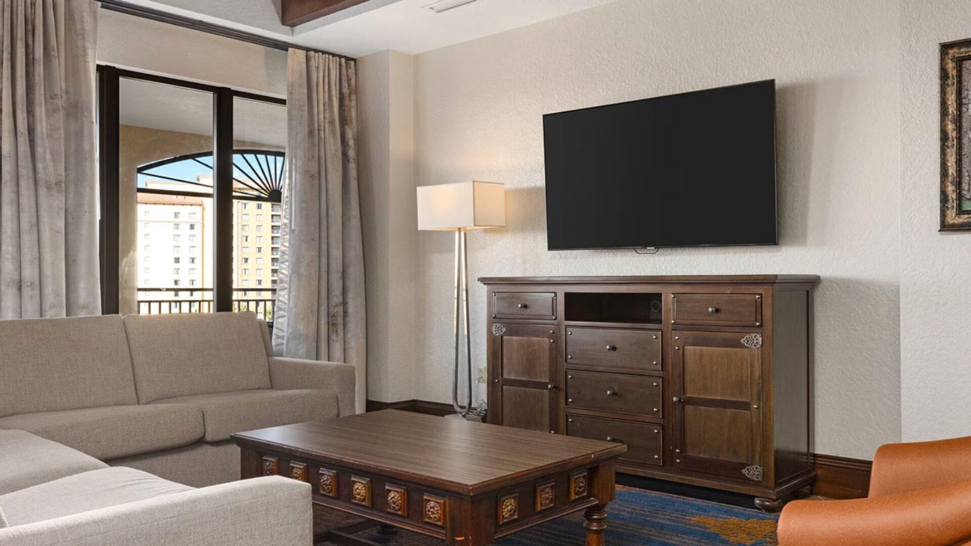 A hotel room with a sofa, armchair, wooden coffee table, and a TV mounted on the wall.