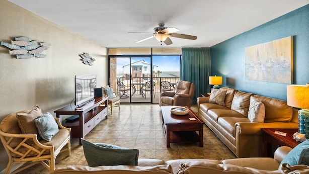 A spacious living room with a balcony, furnished with leather sofas, a coffee table, and a TV.