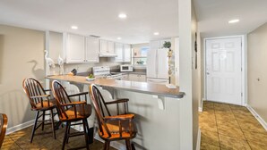 A modern kitchen with white cabinets, a central island with bar stools, and a microwave.