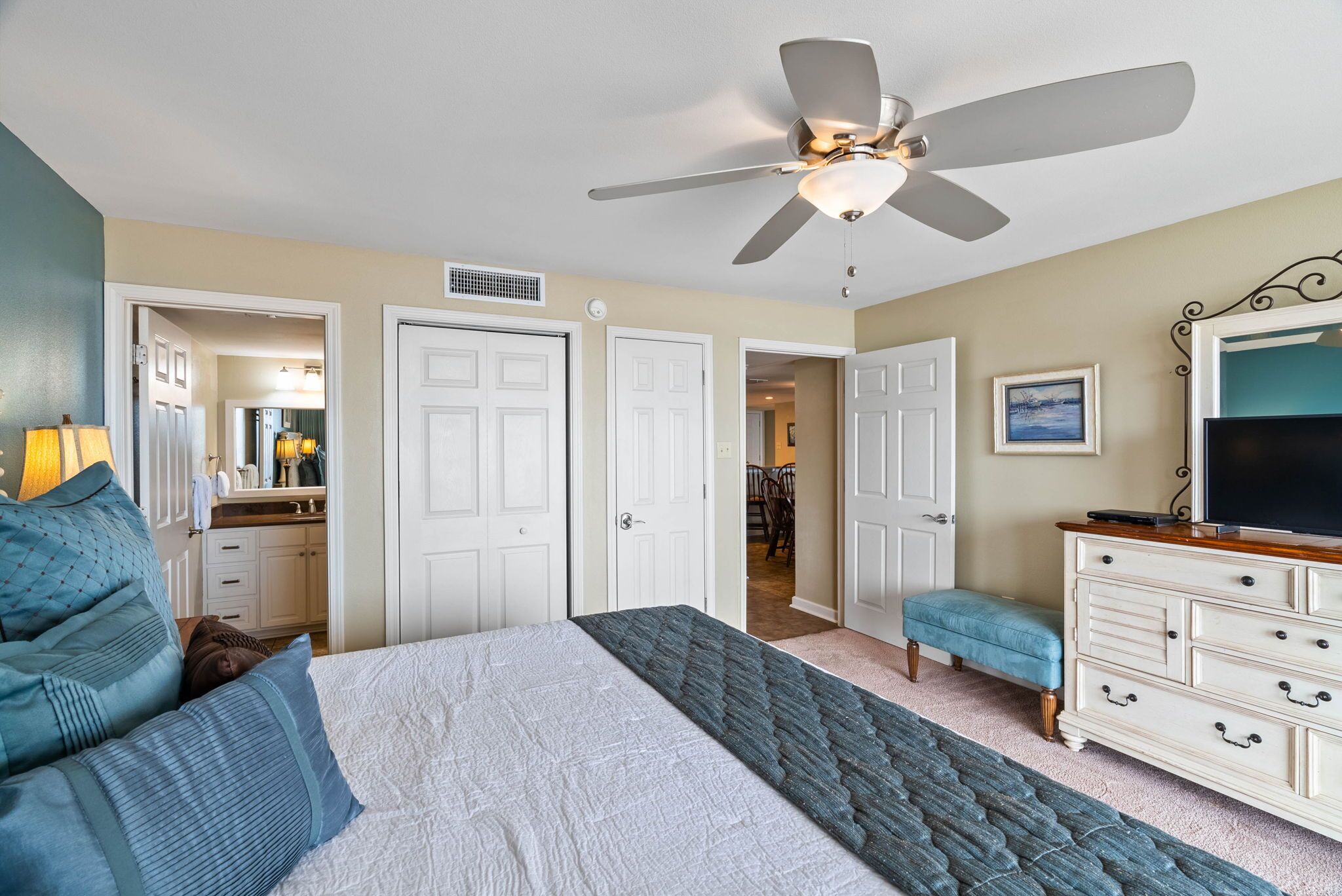 A bedroom with a bed, a ceiling fan, a dresser, and a television.