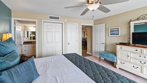 A bedroom with a bed, a ceiling fan, a dresser, and a television.