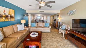 A living room with a beige sofa, a coffee table, a TV stand, and a ceiling fan.
