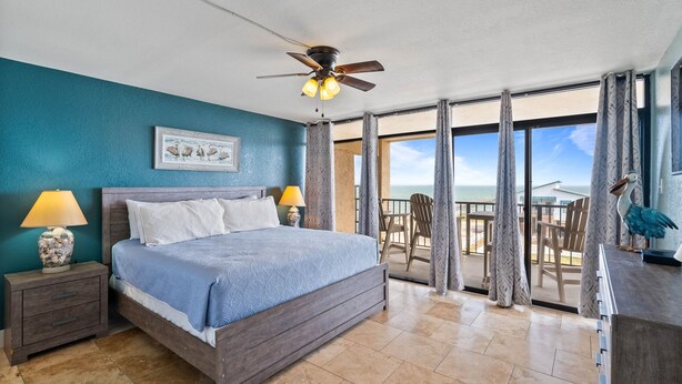 A bedroom with a bed, nightstands, a ceiling fan, and a view of the balcony with outdoor seating. - Welcome to Grandview – Laguna Reef Unit 414 (Rockport)