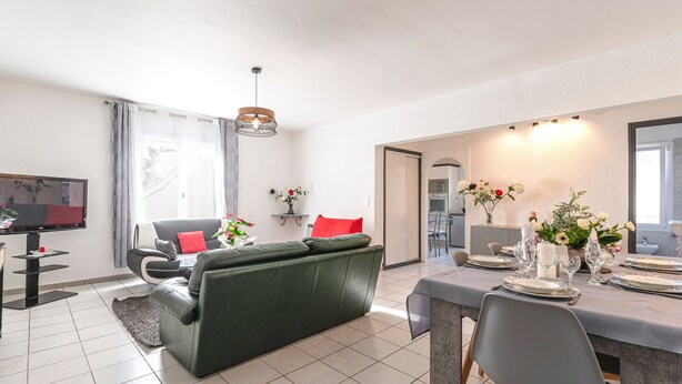 Ein modernes Wohnzimmer mit einem grünen Sofa, einem Esstisch für vier Personen und einem Fernseher in der Ecke.