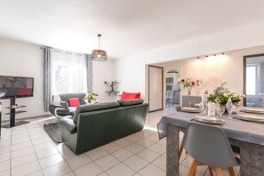 A modern living room with a green sofa, a dining table set for four, and a TV in the corner. - Le Ricci - Climatisé, plages à 2 km (Ajaccio)