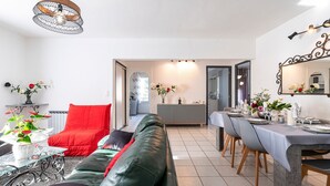 Ein modernes Wohnzimmer mit einem grünen Ledersofa, einem roten Sessel und einem Essbereich mit einem langen Tisch, gedeckt für eine Mahlzeit.
