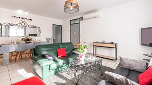 Ein modernes Wohnzimmer mit einem grünen Sofa, einem Glastisch und einem Essbereich für vier Personen.
