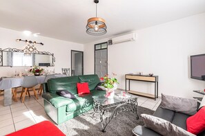 A modern living room with a green sofa, a glass coffee table, and a dining area with a table set for four. - Le Ricci - Climatisé, plages à 2 km (Ajaccio)