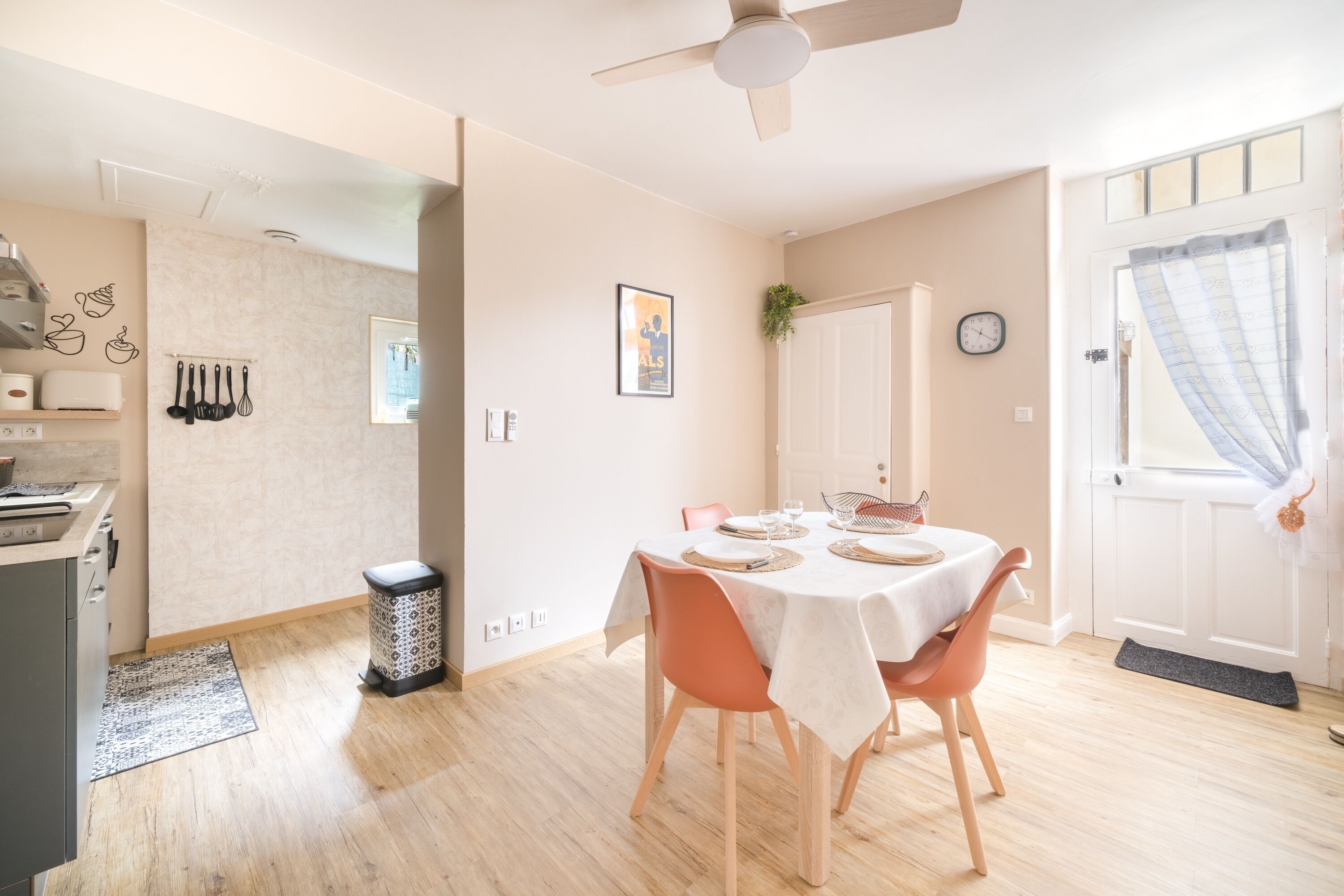 Un coin repas avec une table dressée pour quatre personnes, un ventilateur de plafond et un espace cuisine équipé d’un grille-pain et d’ustensiles.