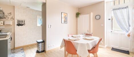Un coin repas avec une table dressée pour quatre personnes, un ventilateur de plafond et un espace cuisine équipé d’un grille-pain et d’ustensiles.