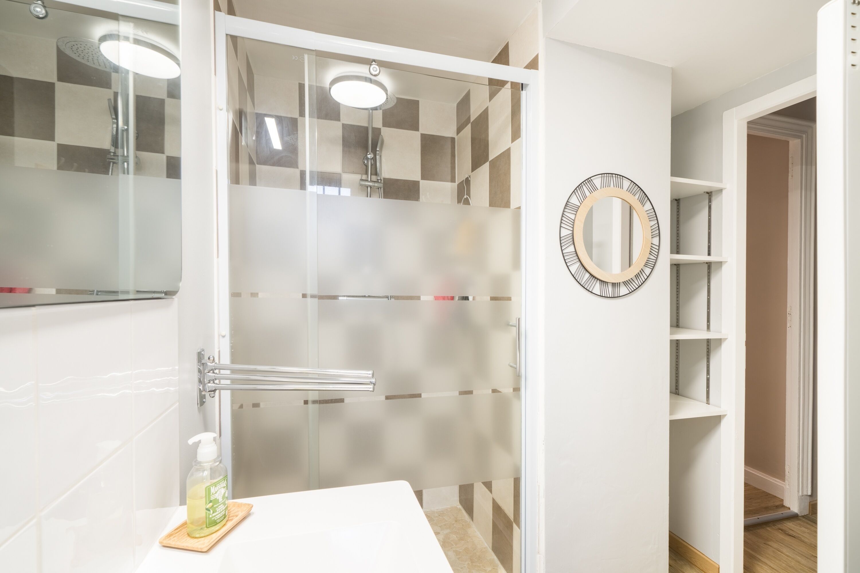 A bathroom with a glass shower enclosure, a white sink, and a mirror on the wall.