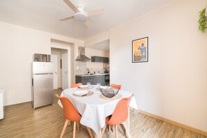 A dining area with a table set for four, a ceiling fan, and a kitchen in the background.