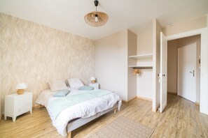 A bedroom with a bed, bedside tables, a hanging light fixture, and a door leading to another room.
