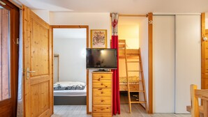 Ein kleines Zimmer mit einem Bett, einem Fernseher, einer Holzkommode und einer Leiter.