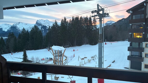 Blick von einem Balkon auf eine verschneite Berglandschaft mit Seilbahn und einem Gebäude mit Balkonen.