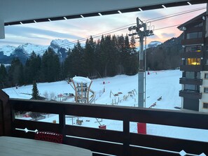 Uitzicht vanaf een balkon op een besneeuwd berglandschap met een skilift en een gebouw met balkons.