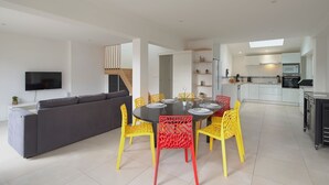Uma sala de estar moderna com sofá cinzento, cadeiras amarelas e uma mesa de jantar posta para quatro pessoas.