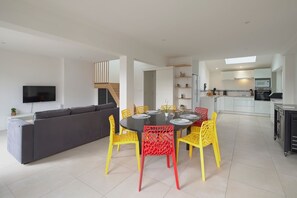 Un salon moderne avec un canapé gris, des fauteuils jaunes et une table à manger dressée pour quatre personnes.