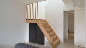 Um interior moderno com escada de madeira que dá acesso a um mezanino, um banco e uma porta para outro cômodo.