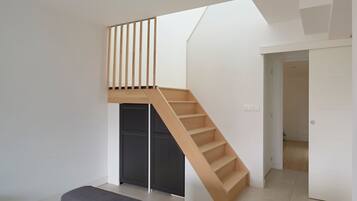 Un intérieur moderne avec un escalier en bois menant à une mezzanine, un banc et une porte donnant sur une autre pièce.