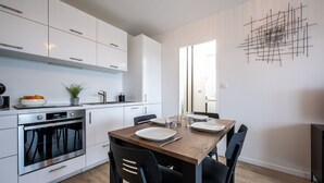 Une cuisine moderne avec des meubles blancs, un four encastré et un coin repas comprenant une table en bois et des chaises noires.