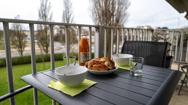Une table de balcon avec une bouteille, des bols, une assiette de croissants et des verres.