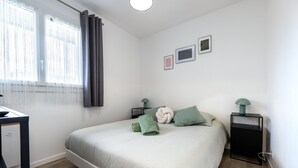 Une chambre à coucher avec un lit, deux tables de chevet, un bureau et une fenêtre avec des rideaux.