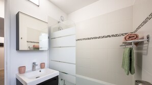 Une salle de bain moderne avec une douche en verre, un lavabo blanc avec deux tasses roses et une serviette verte suspendue à un porte-serviettes.