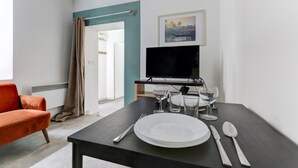 Een moderne woonkamer met een bank, een eettafel gedekt met borden, bestek en glazen, een televisie en een ingelijst schilderij aan de muur.