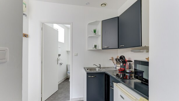 Een kleine keuken met een spoelbak, fornuis en kastjes.
