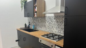 Et kompakt køkken med gasblus, ovn og vask. Der er skabe, en bordplade og et backsplash med mønstret flisebeklædning.