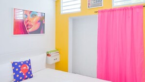 A bedroom with a white bed, a blue polka dot pillow, a pink curtain, and a painting on the wall. - Vibrant Apartment By The Beach (San Juan)
