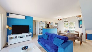 A living room with a blue sofa, a flat-screen TV, and a white entertainment unit. - Beautiful beach apartment with sea view (Grand-Case)