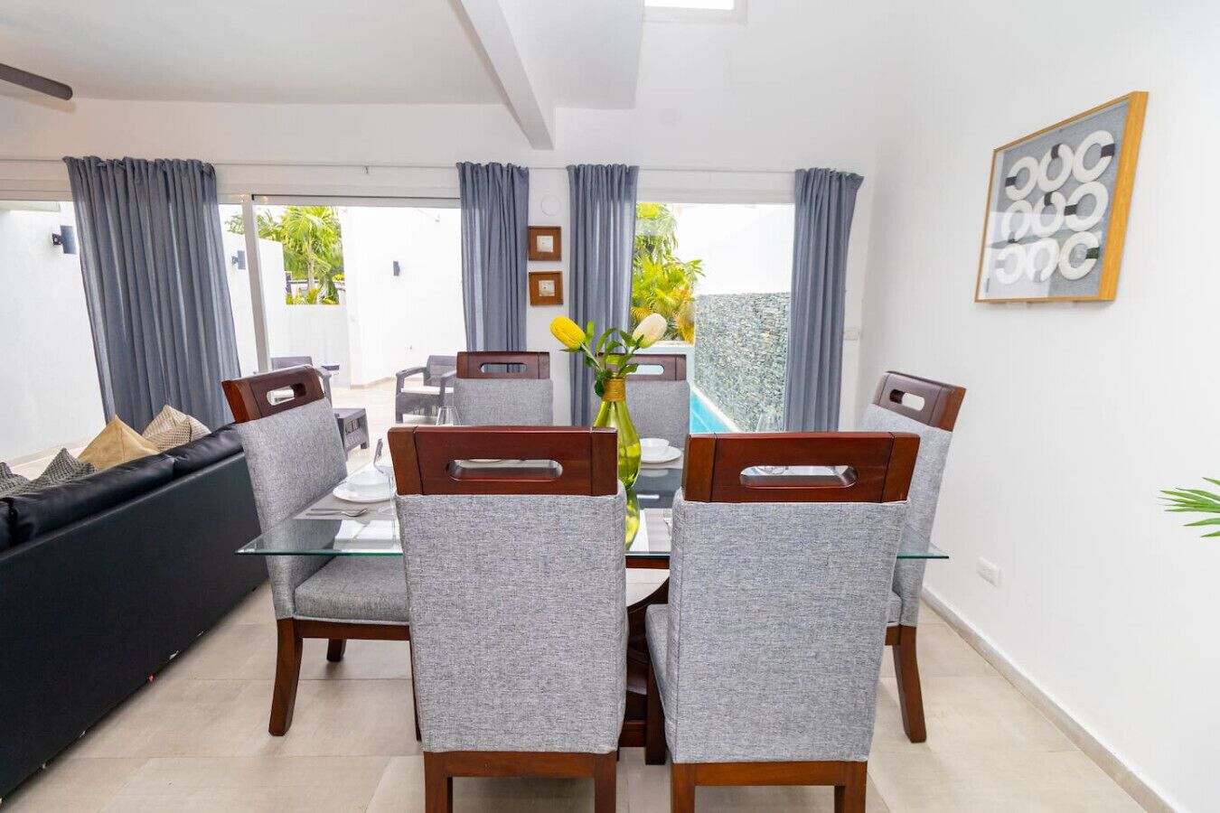 A dining area with a glass table, grey upholstered chairs, and a view of a pool through the glass door.