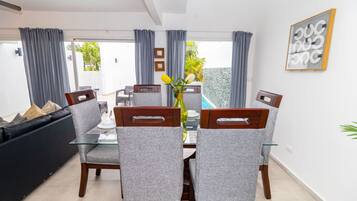 A dining area with a glass table, grey upholstered chairs, and a view of a pool through the glass door.