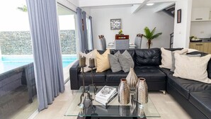 A modern living room with a black leather sofa, a glass coffee table, and a view of a swimming pool. - Tropical 3BR Retreat w/ Private Pool in Bayahibe (San Rafael del Yuma)