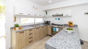 A modern kitchen with white cabinets, a granite countertop, a gas stove, and a microwave. - Tropical 3BR Retreat w/ Private Pool in Bayahibe (San Rafael del Yuma)