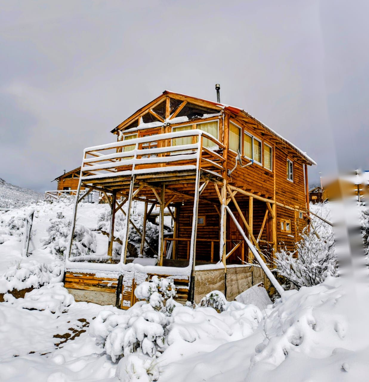 A wooden cabin with a balcony, surrounded by snow.