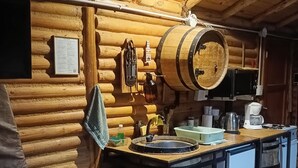 Interior de una cabaña de troncos con una barra de madera, un lavabo y una mesa de comedor de madera.