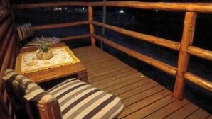 Una terraza de madera con una silla acolchada y una mesita pequeña, con vistas a un paisaje montañoso de noche.
