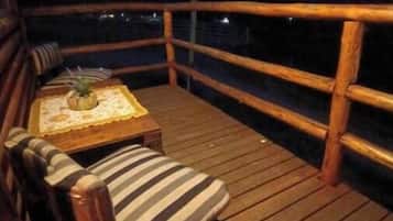 Una terrassa de fusta amb una cadira amb coixí i una taula petita, amb vista a un paisatge montanyós de nit.