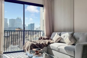 A balcony with a view of city buildings, a grey sofa with cushions, and a glass coffee table with a remote control. - Chic, cozy studio just 2 minutes from Anfa Park and CFC. (Casablanca)
