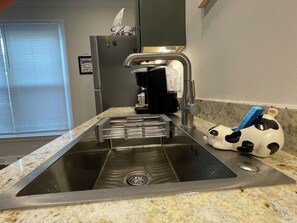 Eine Küche mit Spüle aus Edelstahl, einer Kaffeemaschine und einer Seifenspender in Kuhform.