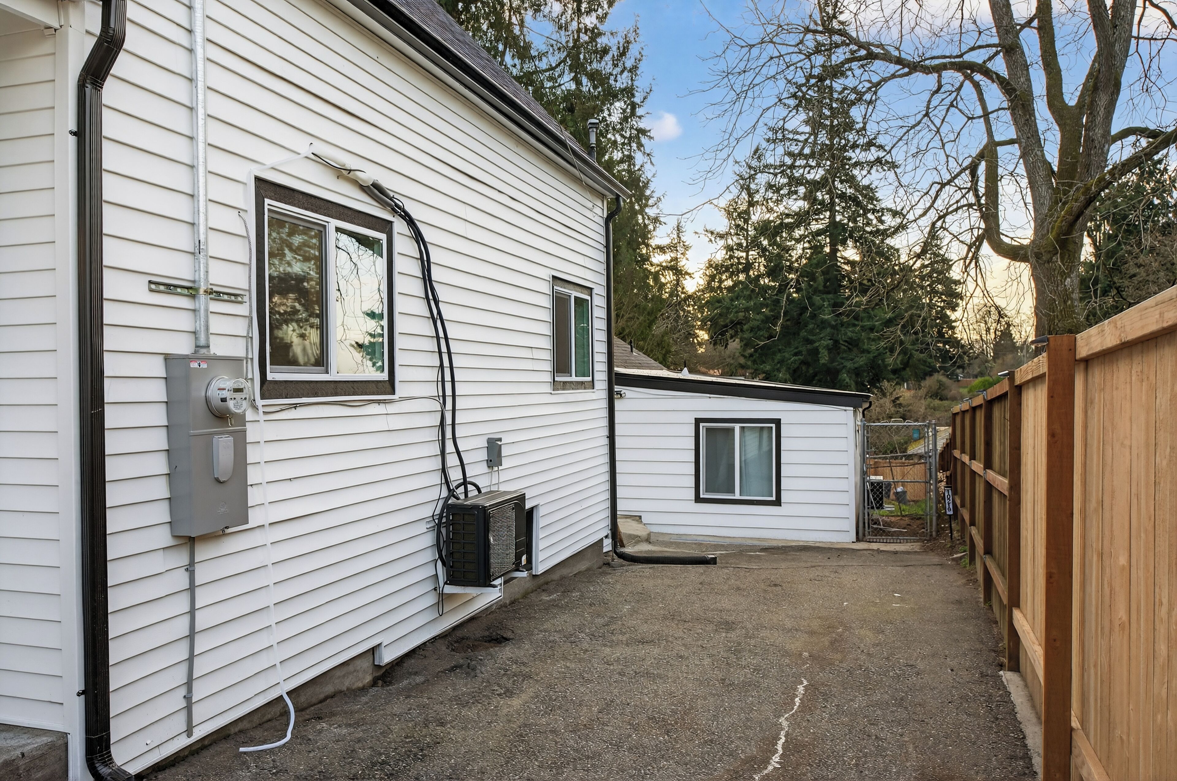 A white mobile home with a small attached garage, a fenced yard, and a large tree in the background.