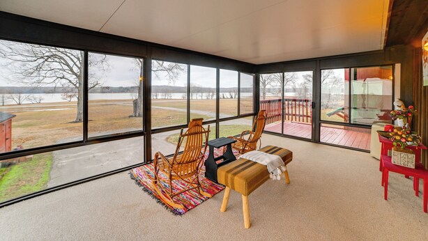 A spacious room with large windows, a wooden rocking chair, a bench, and a small table. - Steps to Shore: Group Getaway on Kentucky Lake! (Hardin)