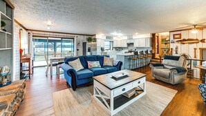 A spacious living room with a blue sofa, a wooden coffee table, and a kitchen area in the background. - Steps to Shore: Group Getaway on Kentucky Lake! (Hardin)