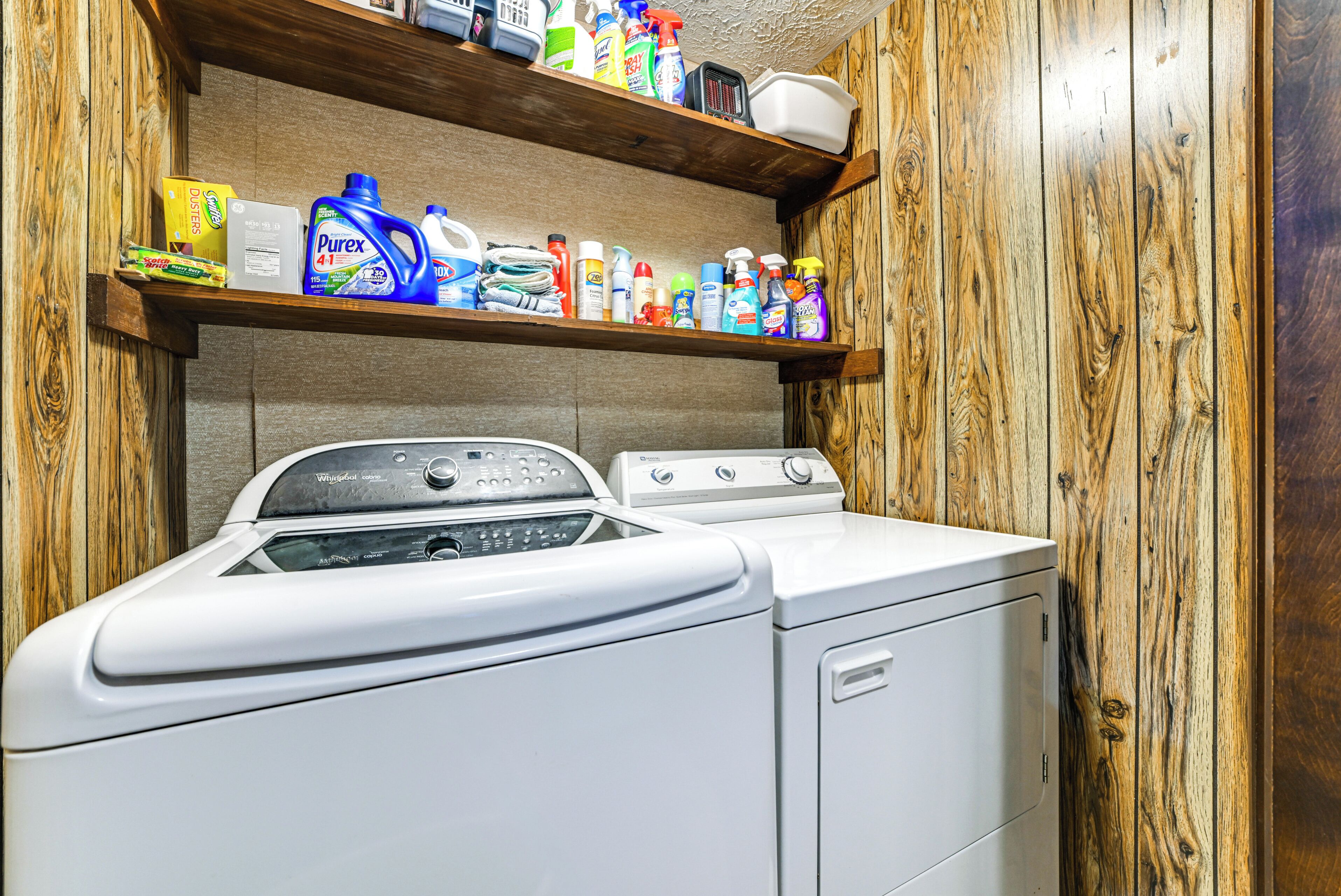 A laundry area with a washing machine and dryer, a shelf with cleaning products, and wooden walls.
