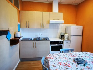 A compact kitchen with a sink, stove, and refrigerator. There is a blue chair and a table with a floral tablecloth. - Charming apartment in La Bourboule, for 4 people, wifi included (La Bourboule)
