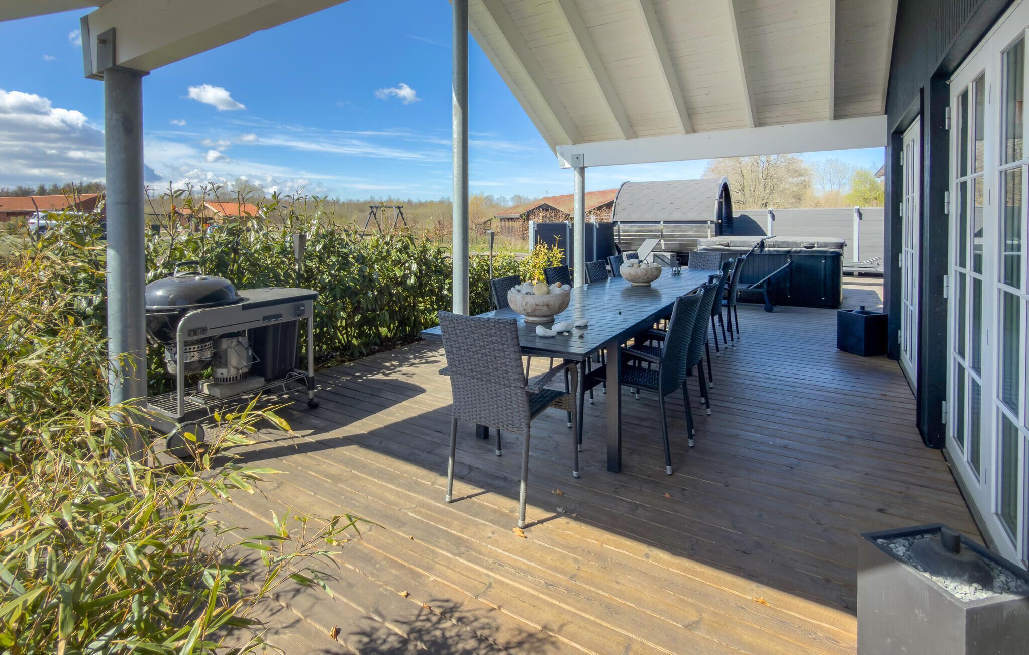 Een terras buiten met een barbecue, eettafel en stoelen.
