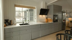A modern kitchen with grey cabinetry, a built-in oven, a stainless steel refrigerator, and a window with blinds. - Nice home in Grenaa with sauna (Grenaa)